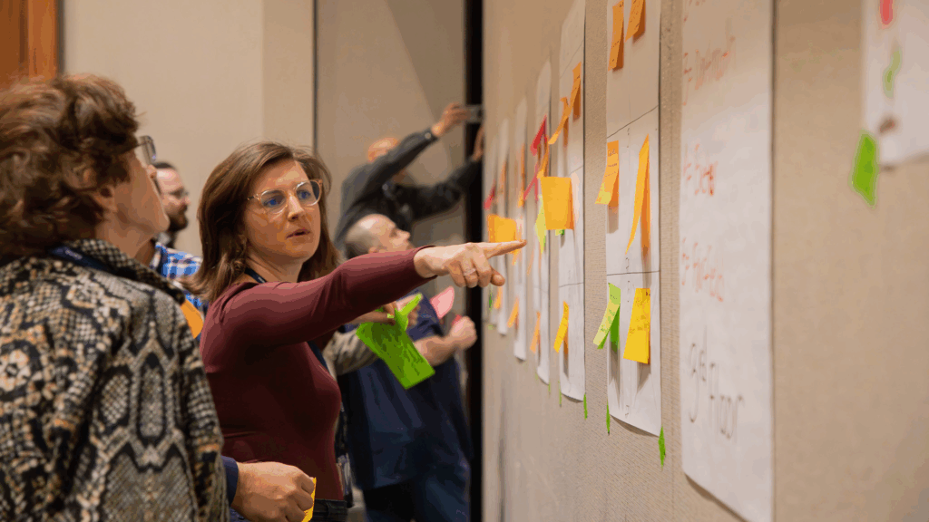 A woman in a maroon shirt points at one section of colorful sticky notes while another woman observes.